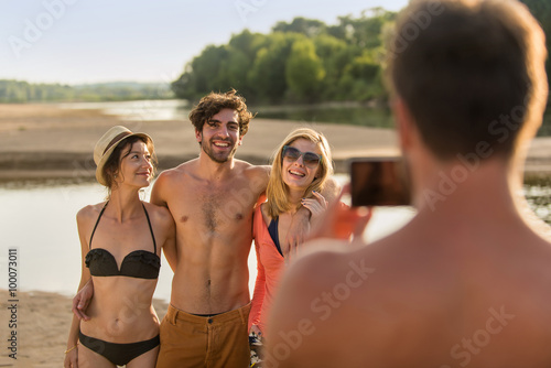 At the beach, one of friends is taking a shot of the others with a smartphone. © jackfrog