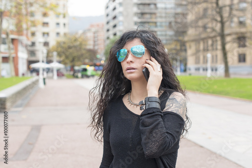 Woman with sunglasses talking by phone in the street.