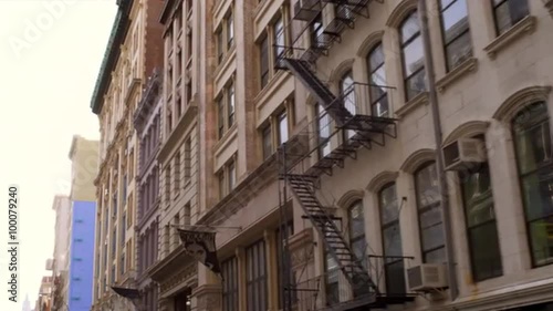 Tracking shot of the side of buildings with fire escapes.