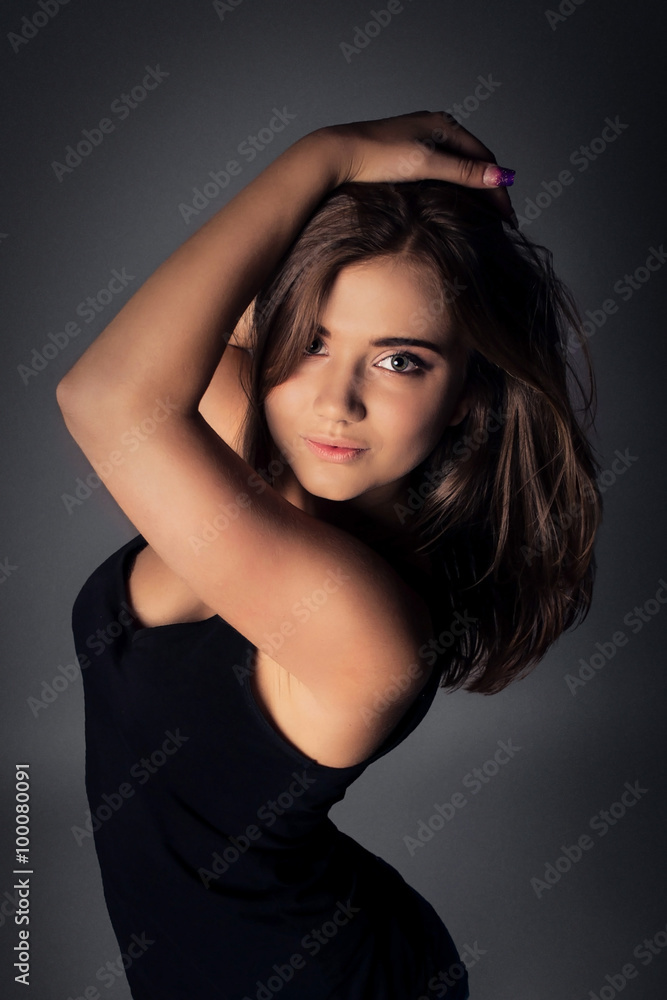 Beautiful seductive brunette girl holds hands hair. Model posing in studio on dark background. Beautiful seductive brunette girl holds hands hair. Model posing in studio on dark background.