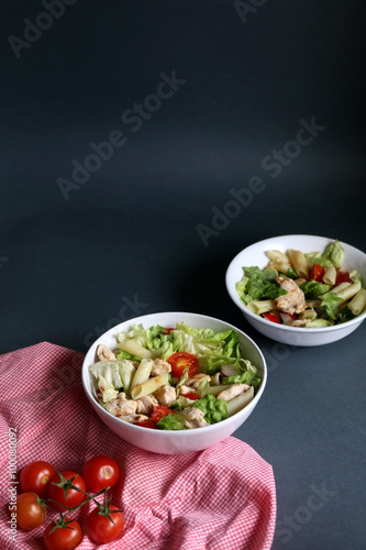 Salad made with lettuce, cherry tomatoes, radish, chicken and pasta. Dark background, selective focus, copy space.
