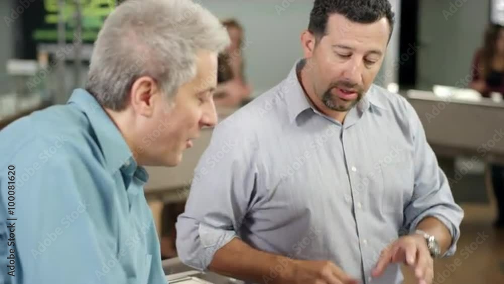 Associate at a recreational marijuana shop talking with an older customer about a product and showing him a large bong Associate at a recreational marijuana shop talking with an older customer about a product and showing him a large bong