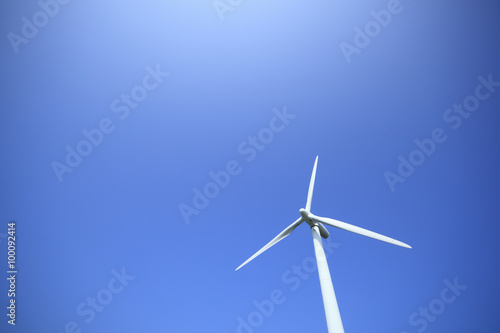 Power generating wind turbine on blue sky with sun. © MP_P