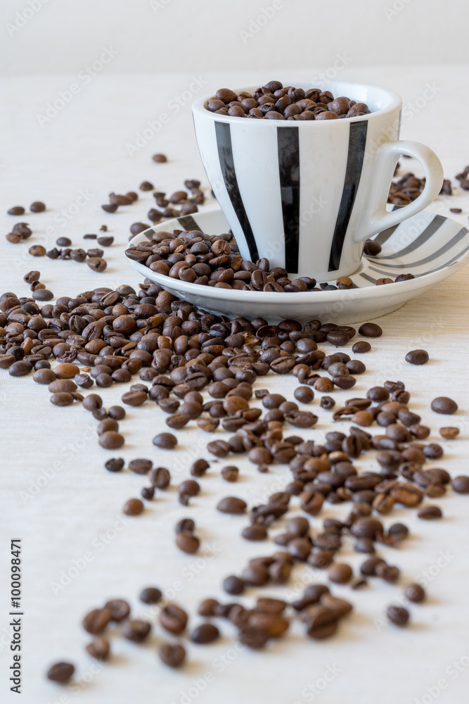 Vertical view of coffee cup filled with coffee beans on white table. Vertical view of coffee cup filled with coffee beans on white table.