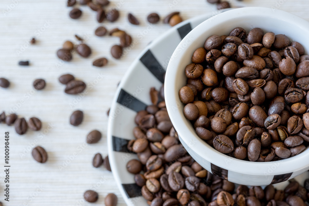 Top view of coffee cup filled with coffee beans on white table. Selective focus. Top view of coffee cup filled with coffee beans on white table. Selective focus.