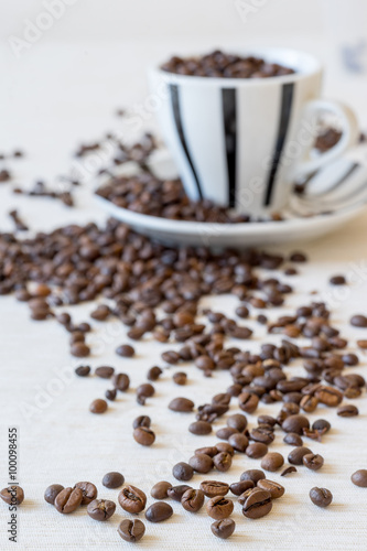 Vertical view of coffee beans with coffee cup in background. Selective focus on beans.