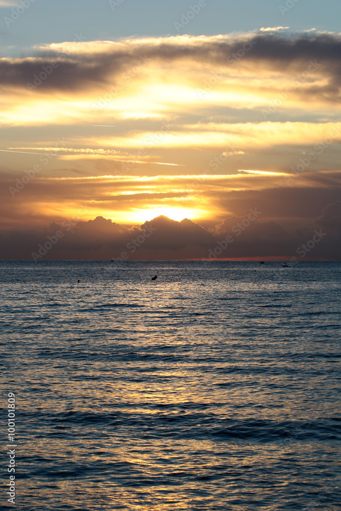 Fototapeta premium Photo of spectacular marine seashore dark blue sea with ripples against yellow-light illumination of low level cloudy sky at sunset time dusk bleakness over seascape background, vertical picture