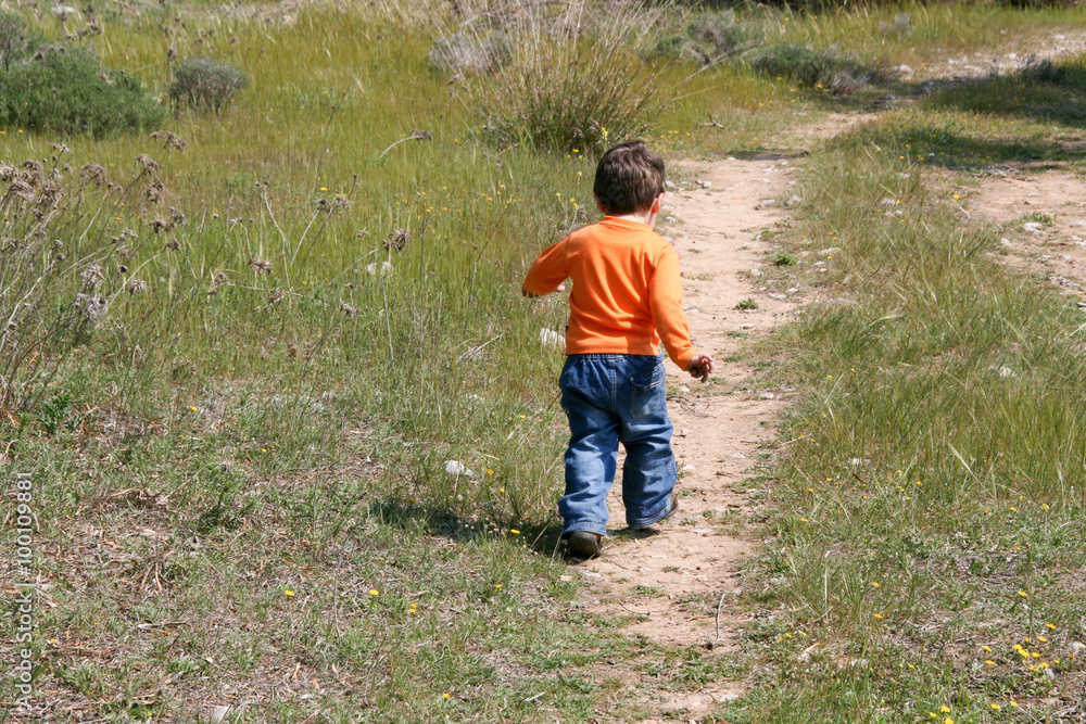 Little Runner.A one year old boy with orange shirt and blue jeans, taking some of his first steps outdoors on a path Little Runner.A one year old boy with orange shirt and blue jeans, taking some of his first steps outdoors on a path