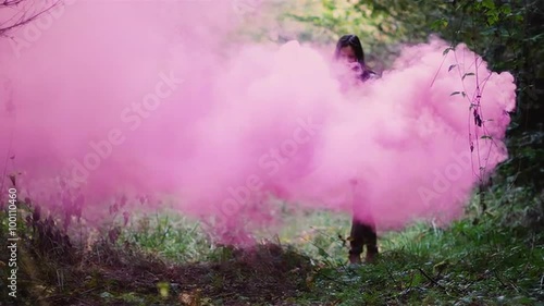 Beautiful girl in a forest runs through pink smoke from a color smoke grenade, slow motion