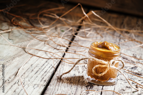 Soft homemade caramel in a glass jar on the old wooden table in photo