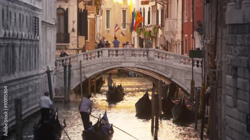 Gondolas traveling with tourists down a golden lite canal with walking bridge in Venice, Italy