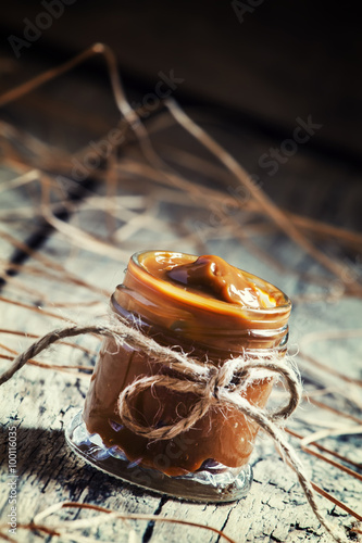 Soft homemade caramel in a glass jar on the old wooden table in photo