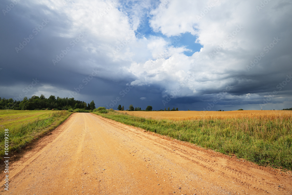 Road and cereal field against dark stormy clouds