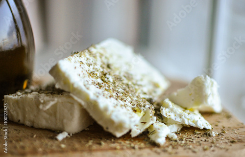 close up of feta cheese(Greek cheese) slices on a wooden serving board  and a bottle of olive oil in nature light