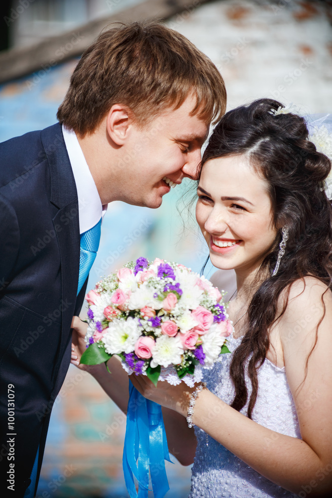 The bride and groom are rolled with laughter, giggle, laugh merrily. Groom in a turquoise tie, he leaned over his wife wearing white wedding dress, holding bouquet. Newlyweds, vertical shot. The bride and groom are rolled with laughter, giggle, laugh merrily. Groom in a turquoise tie, he leaned over his wife wearing white wedding dress, holding bouquet. Newlyweds, vertical shot.
