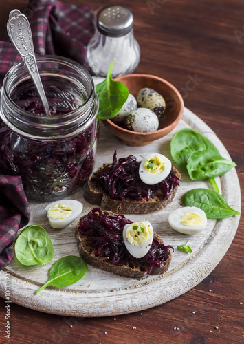 Beetroot relish and a sandwich with beets, quail egg and spinach on rustic light wooden board. Healthy food