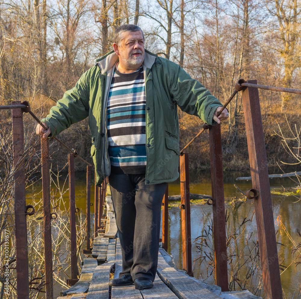 Senior man standing on a suspension bridge over Vorskla river in Ukraine