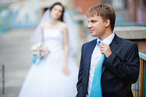 Foto The groom dark blue suit straightens turquoise tie with a sour face, in background tired and frustrated bride waiting
