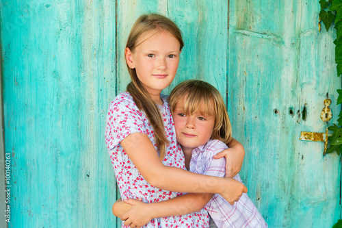 Summer portrait of two cute kids, young girl and her little brother standing against turquoise wooden old door © annanahabed