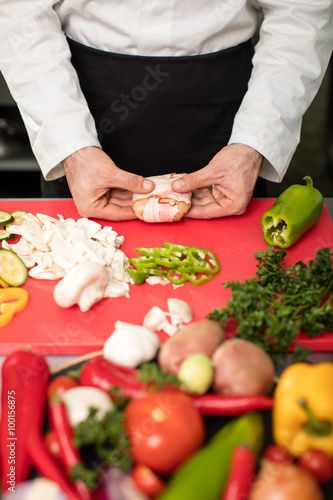 Young chef preparing food and and rolling meat with bacon in big