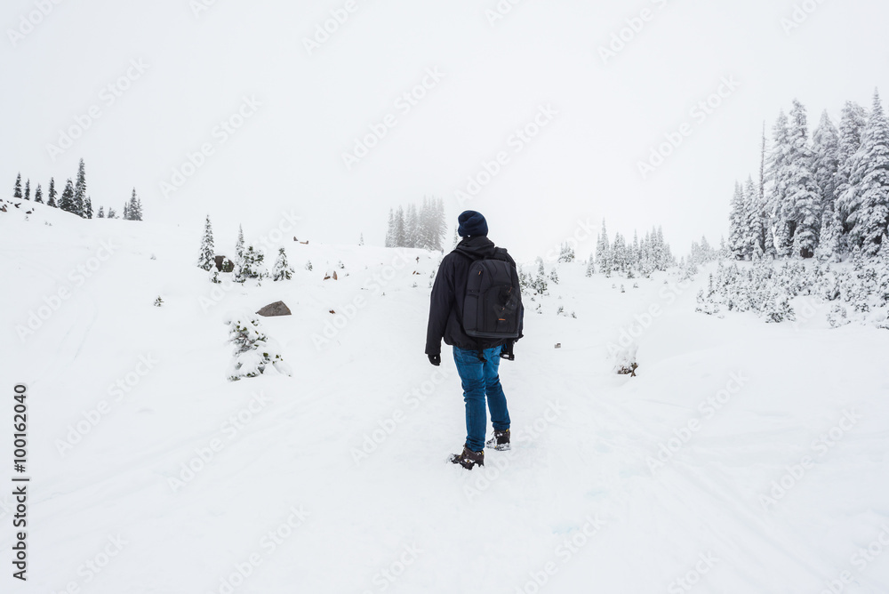 a man stand facing the mountain on a path cover with snow.