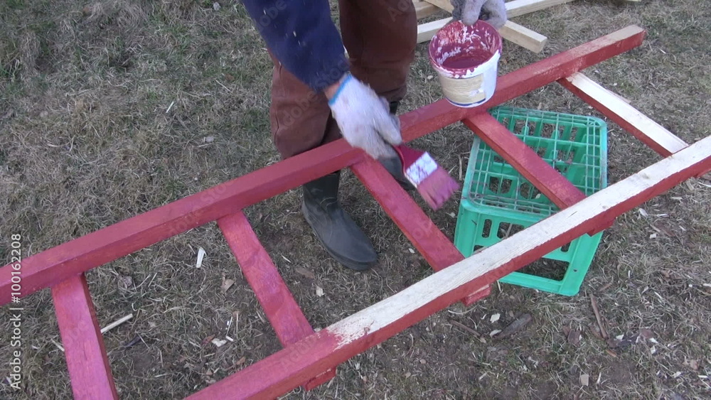 Man farm worker painting wooden ladder red