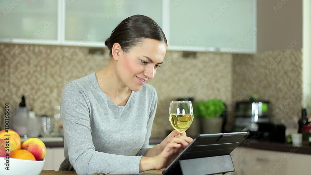 Young brunette woman with glass of wine using a tablet computer in her kitchen Young brunette woman with glass of wine using a tablet computer in her kitchen
