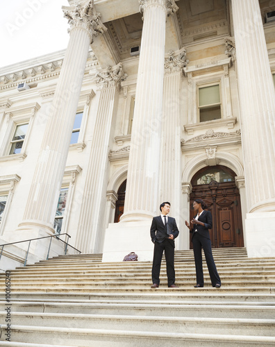 A well dressed man and woman converse on the steps of a legal or municipal building. Could be business or legal professionals or lawyer and client.