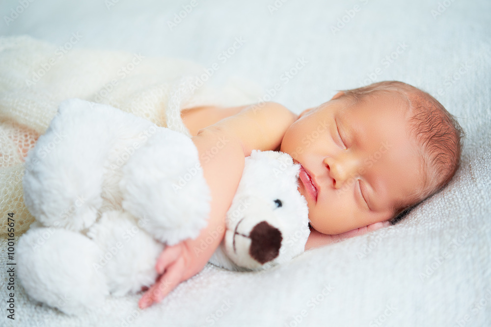 Cute newborn baby sleeps with toy teddy bear