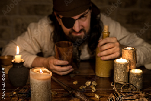 Garstiger Pirat mit Rum sitzt an einem alten Tisch mit vielen Ke photo