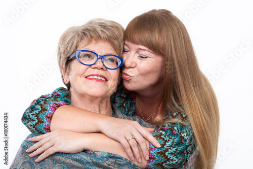 Adult daughter hugging and kissing elderly mother on the cheek, white background