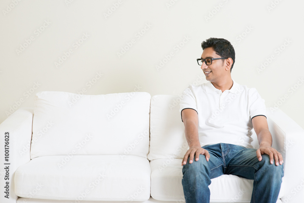 Lonely single Asian man sitting on couch and looking at side