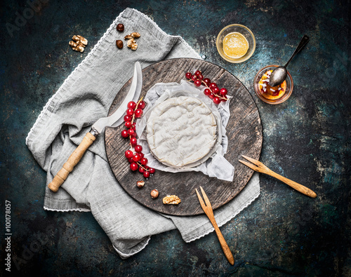 Delicious ripe camembert cheese on wooden cutting board with berries and sauce on rustic background, top view. Traditional milk dairy product
