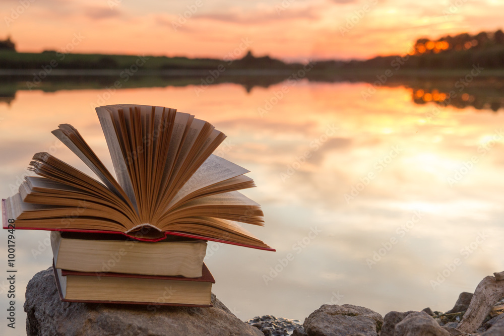 Stack of books and Open hardback book on blurred nature landscape backdrop  against sunset sky with light. Copy space, back to school. Education  background. Stock Photo | Adobe Stock
