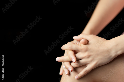 Woman hands fingers crossed on the knee on a black background 