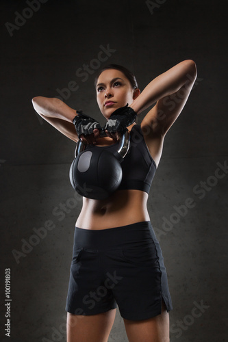 young woman flexing muscles with kettlebell in gym