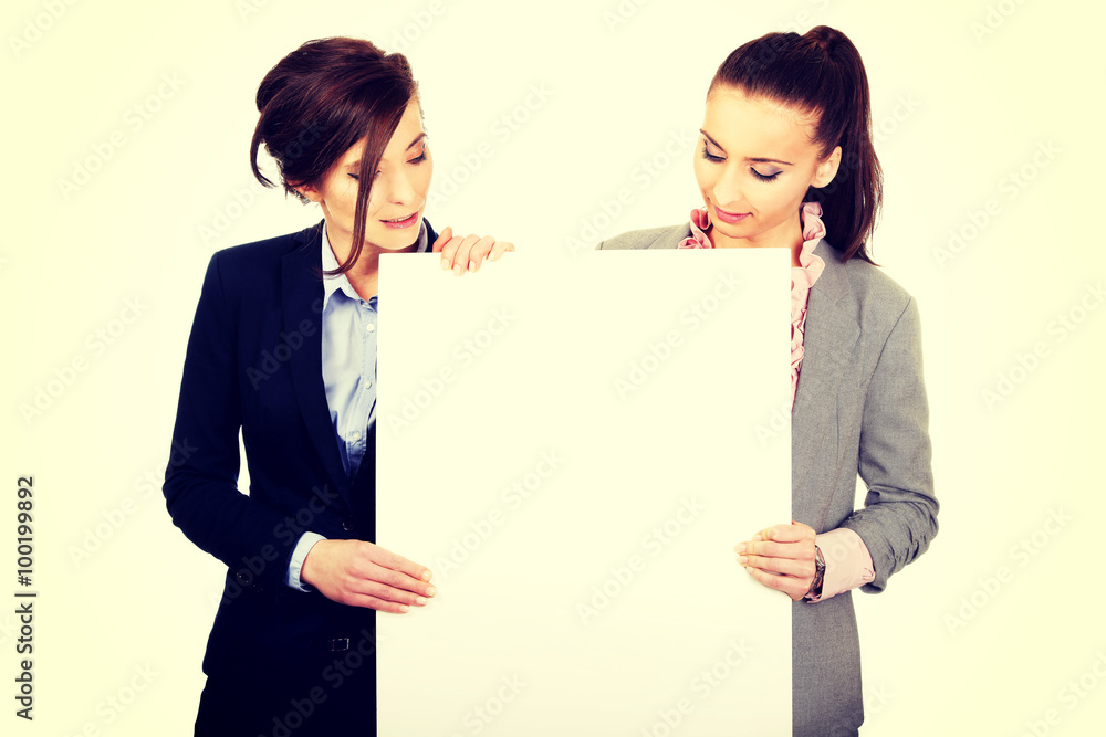 Two businesswomen carrying a big white board. Two businesswomen carrying a big white board.