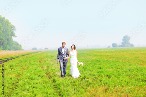 happy beautiful bride and groom walking on field