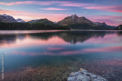 Pink sky at dawn illuminates the peaks reflected in Lake Sils, Engadine, Canton of Graubunden