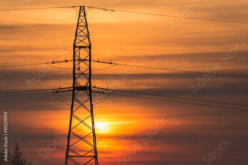 Słup wysokiego napięcia na tle wschodzącego słońca © Piotr Gołębniak