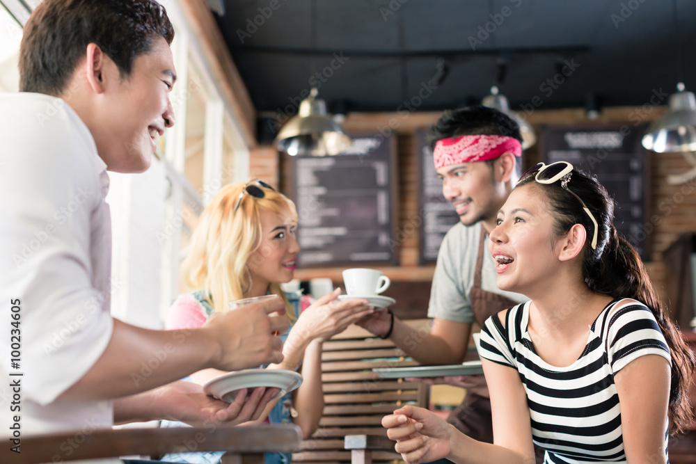 Waiter serving coffee in Asian cafe to women and man Waiter serving coffee in Asian cafe to women and man
