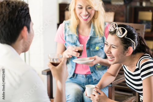 Women and man in Asian cafe drinking coffee