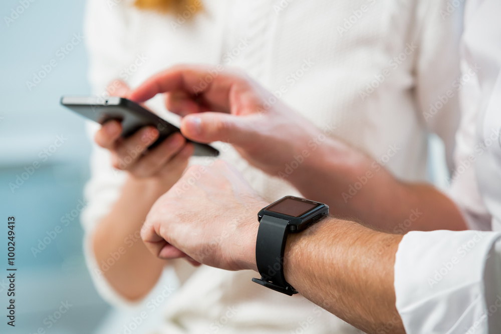 Close up of man and woman hands working on line and synchronising a modern smart watch with smart phone in office Close up of man and woman hands working on line and synchronising a modern smart watch with smart phone in office