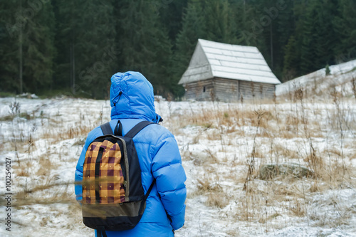 Back side of backpacker man walking to old traditional Carpathian log cabin in Polish Tatra Mountains