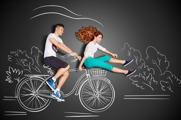 Quick as the wind / Happy valentines love story concept of a romantic couple against chalk drawings background. Male riding his girlfriend in a front bicycle basket.