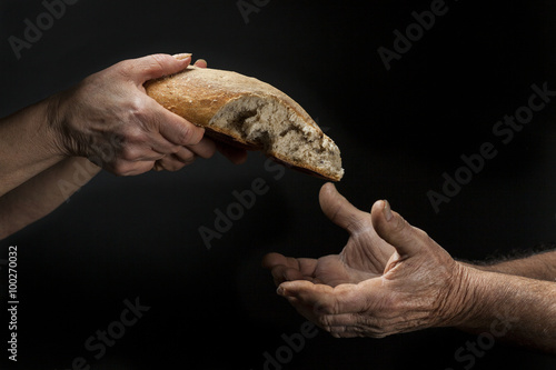 Mano di donna dona pagnotta di pane a un povero senzatetto. Concetto di povertà , emarginazione , fame nel mondo 