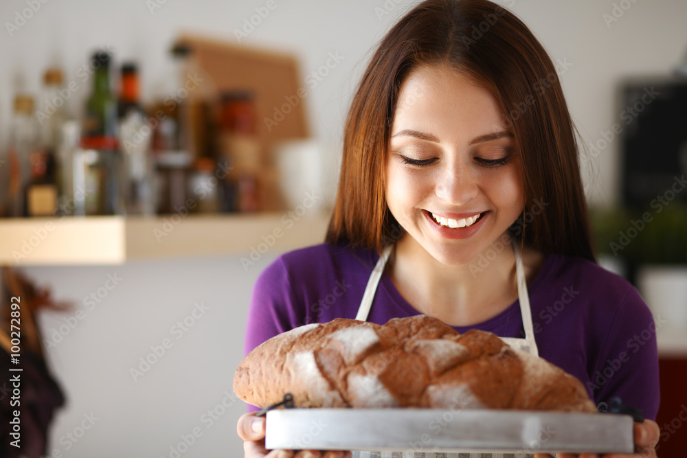 Young woman holding tasty fresh bread in her kitchen Young woman holding tasty fresh bread in her kitchen