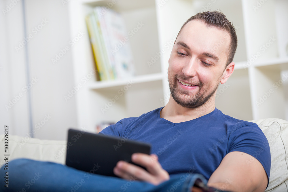 Young Man With Digital Tablet Sitting On Sofa In Living Room Young Man With Digital Tablet Sitting On Sofa In Living Room