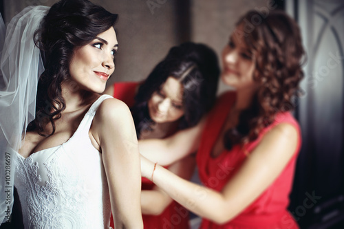 Bridesmaids in red dresses help beautiful bride prepare for her