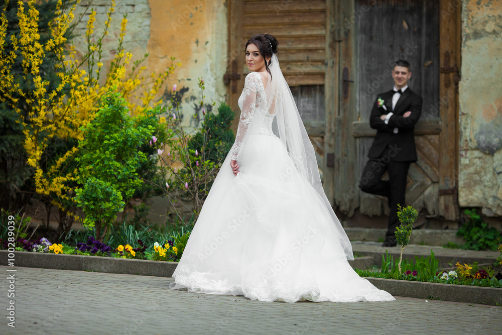 Beautiful brunette bride walking down old street, while the groo Beautiful brunette bride walking down old street, while the groo